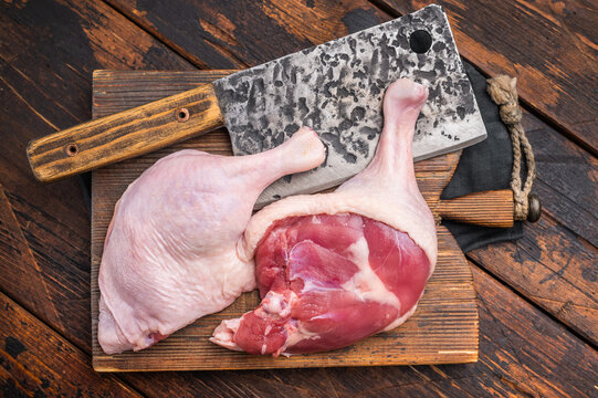 Uncooked duck legs ready for cooking, set on a weathered wooden surface, with a cleaver and rosemary &mdash; warm, rustic tones.