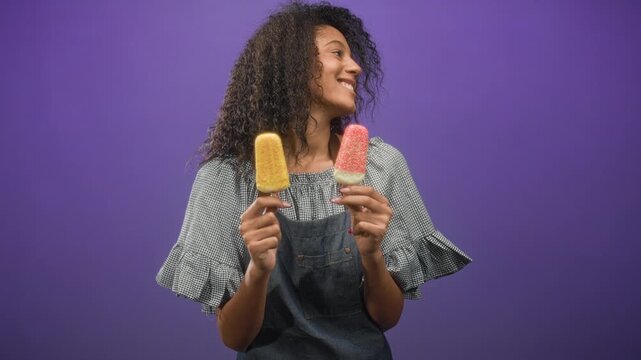 Woman waitress holding two ice cream pops, smiling with hands raised in studio; joyful summer treat.