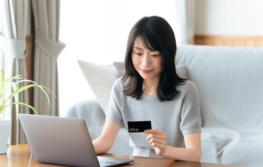 ノートパソコンでクレジットカード決済をする女性の自宅ワークシーン, Woman making a credit card payment on a laptop while working from home