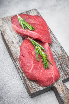 Fresh raw Wagyu chuck steak resembling zabuton or Denver cut arranged with herbs on weathered wood against bright gray backdrop ideal for premium food photography.