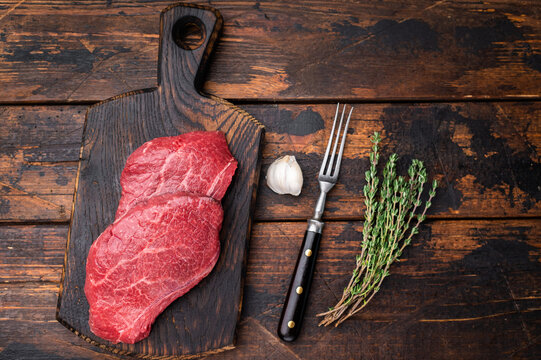 Uncooked Wagyu chuck steak with deep texture placed on rustic board with herbs and garlic over weathered timber surface perfect for butcher content.