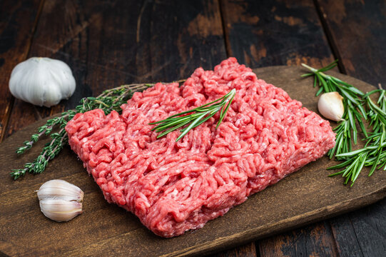 Fresh raw groundmeat with rosemary and thyme on dark wooden board over rustic table ideal for cooking, butcher and protein ingredient themes.