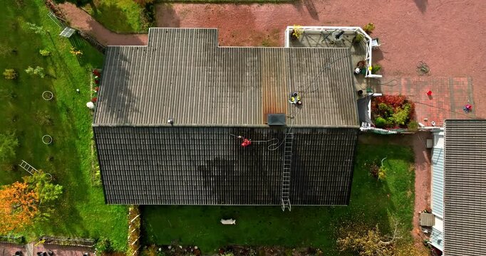 Birds eye drone shot above a house with a person cleaning the roof, fall day