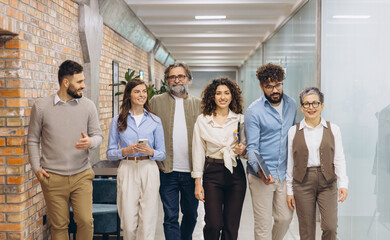 Obraz premium Diverse business team walking through a modern office corridor, collaborating and discussing work