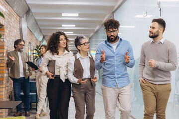 Diverse business professionals walking through office corridor, discussing work, team...