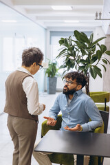 Business colleagues collaborating, discussing project details in modern office lounge area, sharing...