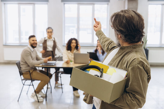 Disgruntled employee leaving office after being fired, carrying personal belongings in box, coworkers reacting to dismissal