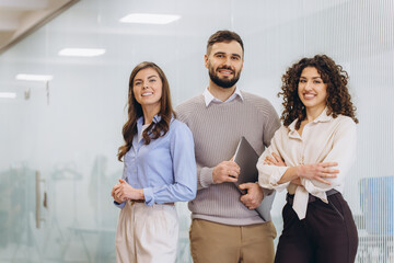 Obraz premium Diverse startup business team standing in modern office corridor, smiling confidently and ready for success