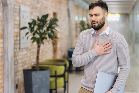 Stressed businessman suffering sharp chest pain, experiencing heart attack symptoms or anxiety in an office