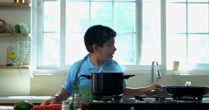 Indian asian young kid cooking tasty soup in pot and making father taste with wooden spoon while smiling together in modern kitchen, playful family bonding and learning moments at home