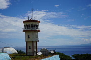 An airport control tower overlooking a coastal landscape under a bright blue sky with scattered clouds.