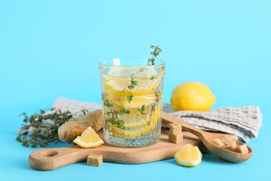 Glass of fresh lemon infused water with ginger and thyme on blue background