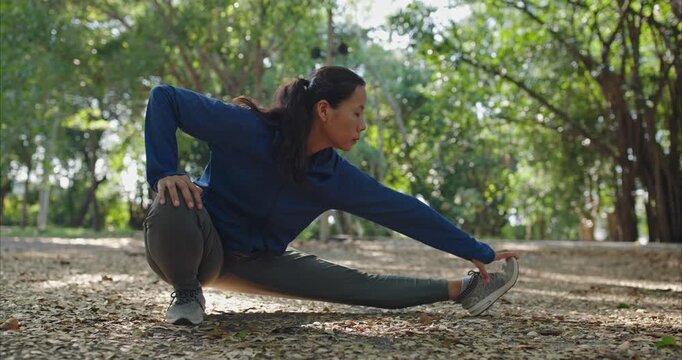 Active Aging Asian Woman Sitting and Stretching with Good Posture, Green Trees Background with Dappled Sunlight for Longevity and Wellness