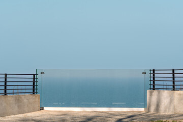 Naklejka premium Minimal seaside terrace with glass railing and wide blue sky, calm backdrop for luxury real estate, travel escape, or wellness ads.