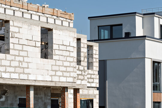 Unfinished masonry shell stands beside completed modern house in sunlight, sharp contrast of construction phases and investment risk.