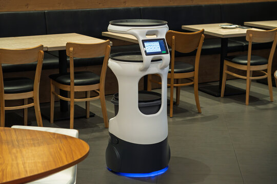 Self-driving waiter robot stands in modern cafe dining area, supports contactless service and faster order delivery with touchscreen.