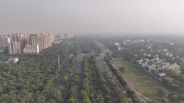 Drone shot over Pari Chowk capturing symmetrical roads, lush green medians, and high-rise apartments in the distance, reflecting Greater Noida&rsquo;s structured planning and expanding skyline.