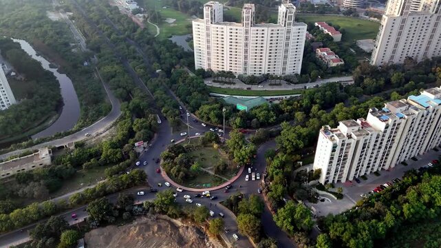 Cinematic aerial view of Delhi Swarn Nagri Road with parallel apartment blocks, lush green corridors, and expanding urban development, capturing the scale and structure of Greater Noida city.