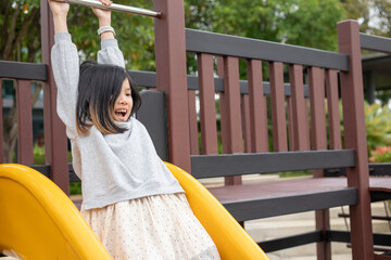 Excited Asian girl sliding quickly down a bright yellow playground slide, shouting with joy and adrenaline © Kwangmoozaa