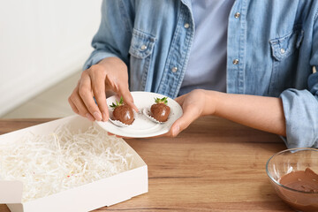 Fototapeta na wymiar Young woman putting chocolate covered strawberries into box at home