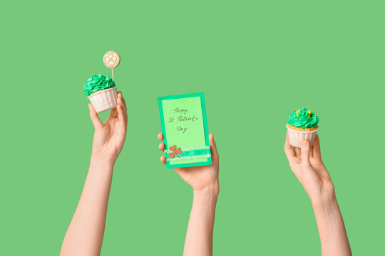 Female hands with tasty cupcakes and festive postcard for St. Patrick's Day on green background