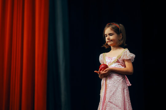 Little Actress Holding an Apple on Stage Playing her Role. Young leading actor with a red apple during a theatrical play 