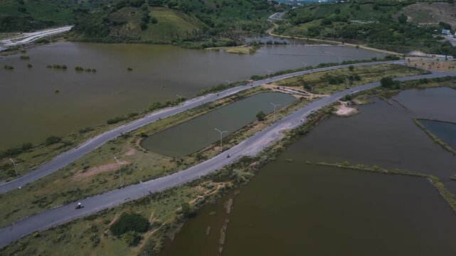 Aerial Coastal Road Over Saltpan Embankments And Pond Networks, Causeway Curves Through Wetland Basin, Remote Corridor For Transport And Local Access, Seasonal Water Patterns And Levees Visible