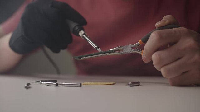 Technician using soldering iron and holding pliers while working on sodimm ram module, generating wisps of smoke during precise task of electronic repair on workbench, close-up, slow motion.