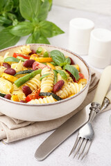 Bowl of tasty pasta salad with tomatoes and basil on white background