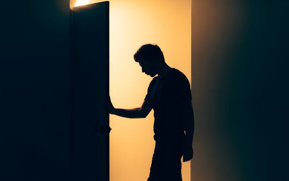 A man in silhouette opening a door to a brightly lit room
