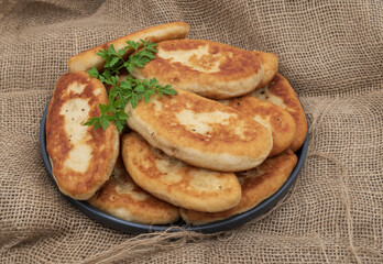 Golden fried potato pies arranged on a plate with fresh parsley. Classic homemade comfort food photographed on rustic burlap fabric, ideal for traditional cuisine and cooking themes.