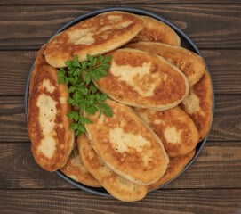 Golden fried potato pies arranged on a plate with fresh parsley. Classic homemade comfort food photographed on rustic wooden background for culinary use.