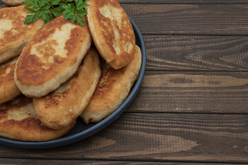 Golden fried potato pies arranged on a plate with fresh parsley. Classic homemade comfort food photographed on rustic wooden background for culinary use.