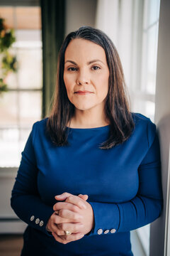 Professional woman standing with clasped hands by window