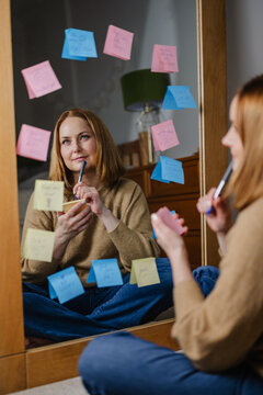 Woman reflecting on positive affirmations with sticky notes on mirror