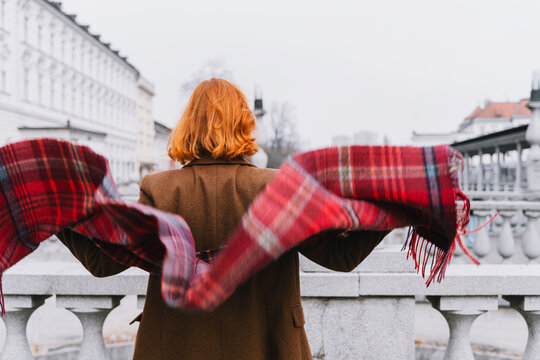 Red-haired woman spreads scarf playfully on urban bridge outdoors