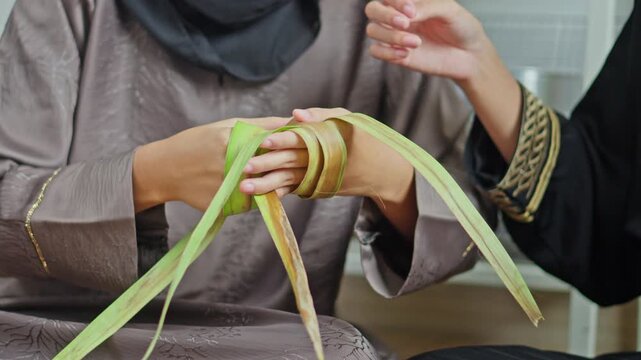 Close up of Two Muslim women sharing tradition of weaving Ketupat pouches for festive Lebaran meals