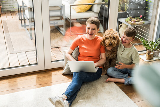 Smiling woman with child and dog using notebook in cozy home setting