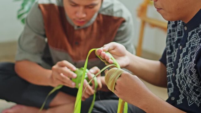 Close-up of muslim men hands preparing traditional rice cakes (Ketupat) by hand-weaving coconut leaves 