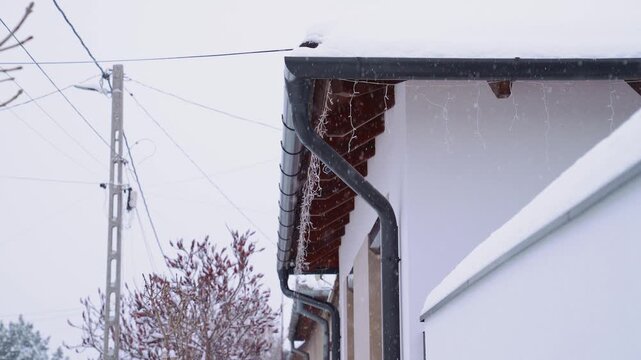 Building roofline detail with snow cover, icicle lights, and a gutter system during a cold day