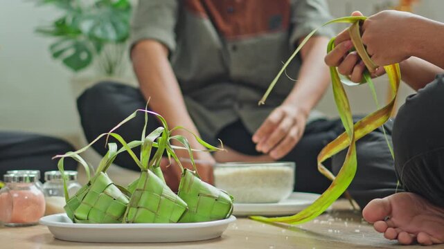 Close-up of finished ketupat pouches on plate with people weaving in background