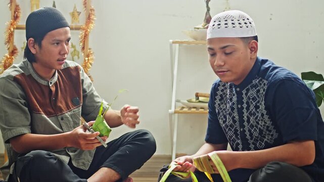 Two Muslim brothers in skullcaps sitting on the floor weaving and trimming traditional Indonesian ketupat leaf pouches
