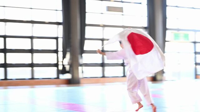 日の丸を掲げて走る空手着の小学生の女の子　スポーツの応援と勝利のイメージ