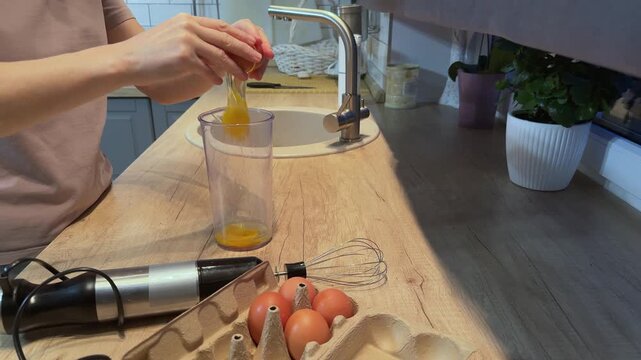 Close up of hands breaking fresh eggs into a plastic cup on kitchen countertop for cooking omelette pancakes or homemade food Warm home kitchen atmosphere Concept of simple home cooking food