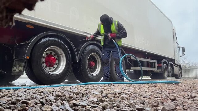 Worker in safety gear pressure washing the wheels and chassis of a large white semi trailer