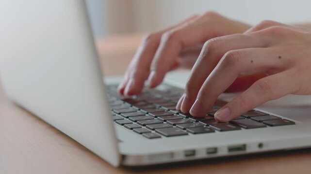 Woman&rsquo;s hands typing on laptop at a wooden desk