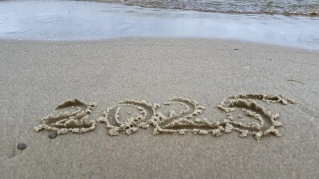 Number 2025 written on wet sand as sea water approaches and erases it. Symbol of time passing endings and letting go. Concept for new year reflection change transition and renewal campaigns.