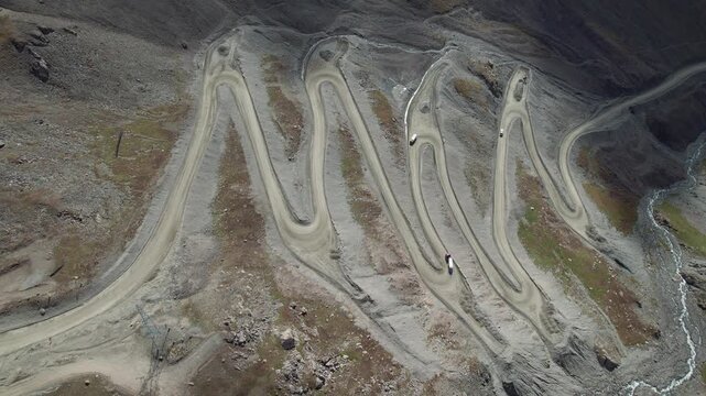 Aerial drone footage of trucks ascending and descending a winding serpentine road carved into an arid mountain landscape in remote Kyrgyzstan. 