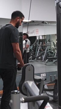 Athletic man performing triceps pushdown exercise using a cable machine with a rope attachment. Bodybuilder strengthening arm muscles in the gym