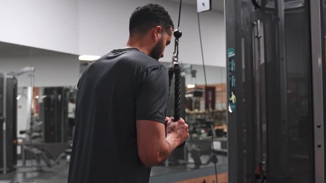 Strong athletic man performing triceps pushdown exercise using a rope attachment on a cable machine. Determined bodybuilder working out